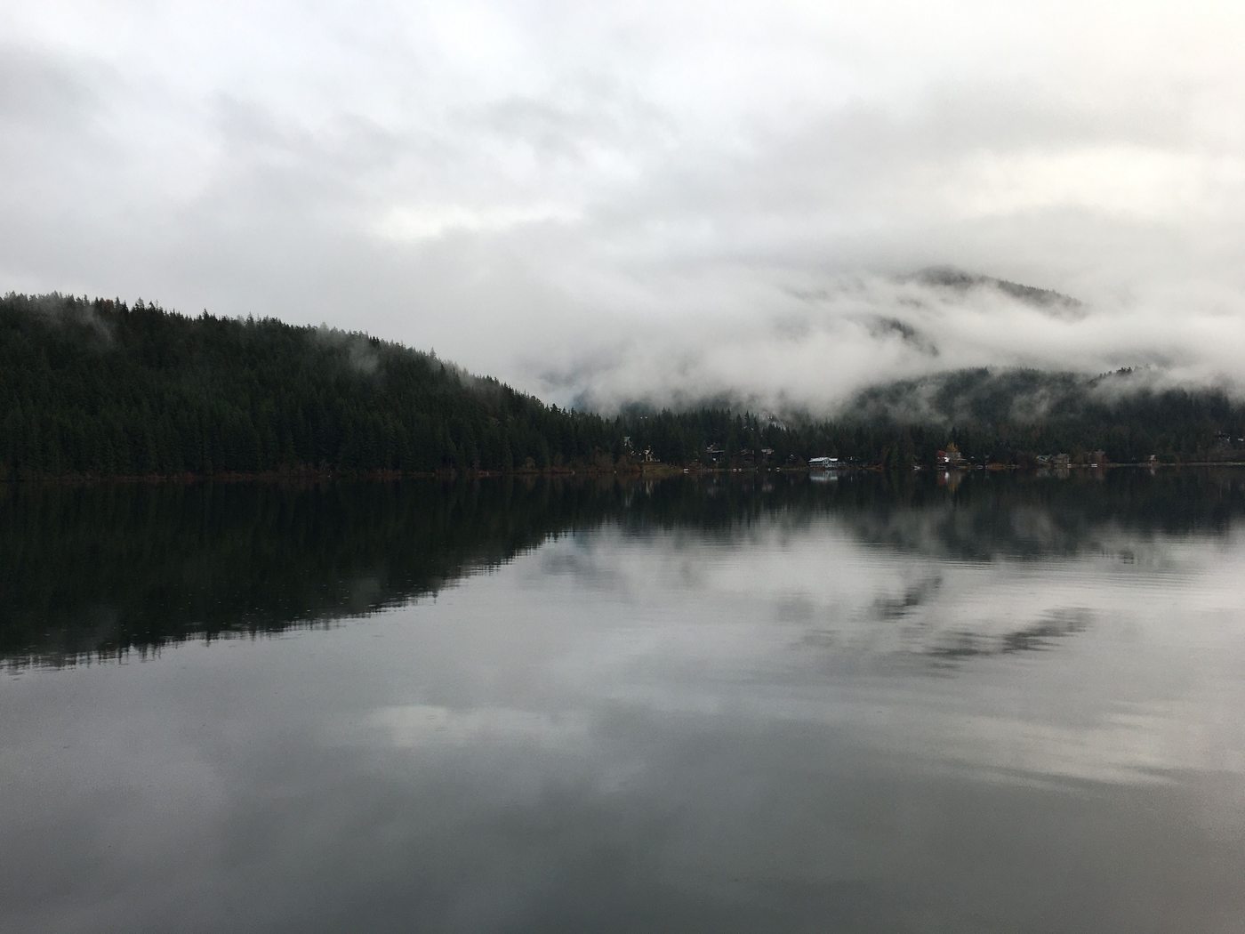 Low clouds over a still mountain lake and forested foothills