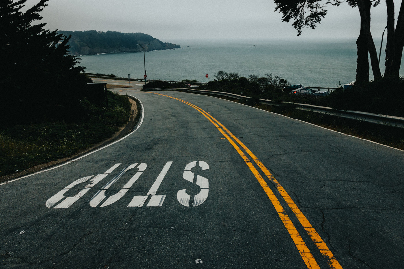 A winding asphalt road with coastal ocean views under an overcast sky